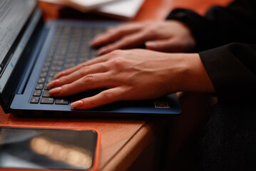 Hand of young female teacher or student typing on laptop keyboard while sitting by desk in front of camera and answering task questions