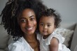 © VICHIZH - Smiling mother holding her baby girl, both with curly hair in a cozy indoor setting