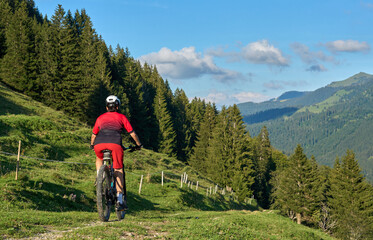 Wall Mural - pretty senior woman riding her electric mountain bike and enjoying the spectacular view over the Allgau alps below the Nagelfluh mountain chain next to Steibis, Bavaria, Germany
