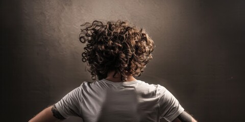 Poster - Young man with curly hair stands with back turned in dimly lit room