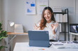 © amnaj - Smiling asian businesswoman is showing ok sign gesture while having video call on tablet in the office
