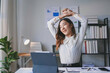 © amnaj - Young businesswoman is stretching her arms at her desk in her office, taking a break from work