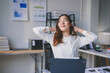 © amnaj - Young businesswoman stretching her neck and back while sitting at her desk in a modern office