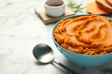 Wall Mural - Tasty mashed sweet potato in bowl and spoon on white marble table, closeup. Space for text