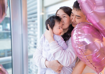 family of three, a man and two women, are hugging a baby