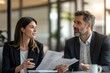 © thanatpong - Business professionals discussing documents in a modern office setting.