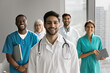 © fizkes - Head shot of ambitious young 35s Arabian male doctor wear white coat posing with group of diverse workmates in modern office. Healthcare field professionals, clinic staff members portraits, medicine