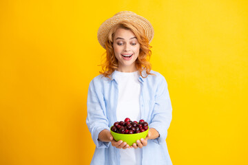 Poster - Young woman eats sweet cherries. Portrait of a beautiful girl with cherry on yellow background. Summer fruit picking season. Natural vitamins.