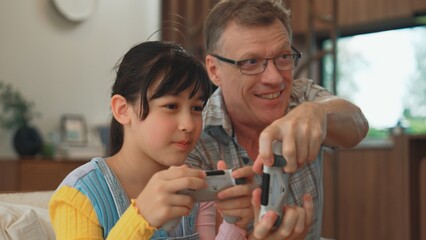 Grandfather and granddaughter together play console game, entertainment media. Old senior use technology communicate with new generation kid cross generation gap strengthen family bond. Divergence.