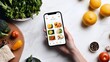 © kinara art design - Person holding a phone displaying a food app, surrounded by fresh vegetables, fruits and spices on a white marble table.