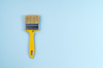 Yellow building brush for walls painting on a blue background, individual housing construction concept