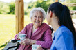 © Halfpoint - Female caregiver spending time with elderly woman, drinking coffee and talking. Nurse and senior woman in wheelchair enjoying a warm day outdoors.