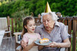 © Halfpoint - Granddaughter celebrating birthday with elderly grandma, blowing candle on cake. Senior lady spending time with young girl, enjoying together time.