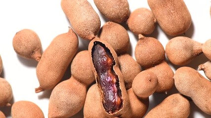 Canvas Print - Tamarind tropical fruits background. Heap Fresh ripe dryed Tamarind pods (Tamarindus indica, Indian date), healthy vegan food. Top view, flat lay, rotating, slow motion