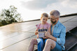 © Halfpoint - Daughter and father on roof with solar panels, holding model of house with rooftop photovoltaic system. Sustainable future for next generation.