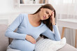 © Prostock-studio - Pregnant Lady Having Headache Touching Head Sitting On Couch Indoor. Migraine During Pregnancy Concept