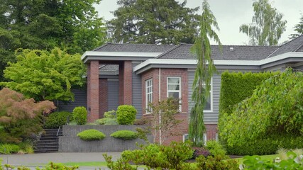 Wall Mural - Establishing shot of two story stucco luxury house with big tree and nice landscape at spring rainfall in Vancouver, Canada, North America. Day time on June 2024. ProRes 422 HQ.