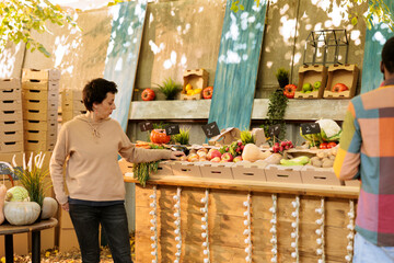 Wall Mural - Multicultural consumers gather near the greenmarket booth to examine seasonal homegrown food products. A young black man and a Caucasian woman go shopping for fresh fruits and vegetables.