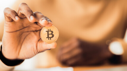 Poster - Digital Currency. African businessman holding golden bitcoin, close up of hand. Panorama, selective focus