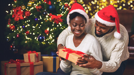 Sticker - My personal Santa. Happy black woman receiving Christmas gift from her caring boyfriend while sitting near Xmas tree at home