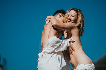 Joyful couple hugging and smiling under a clear blue sky, symbolizing happiness and love in a romantic relationship.