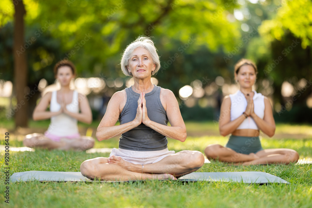 Happy slim mature woman making yoga meditation in lotus pose with group ...