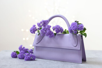 Poster - Stylish violet bag and ageratum flowers on gray table against light background