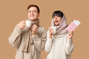 Poster - Beautiful young happy couple with passport, tickets and cups of coffee on brown background. Winter vacation concept