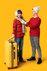 Poster - Beautiful young happy couple with suitcase, passports and tickets on yellow background. Winter vacation concept