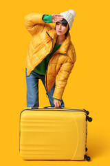 Sticker - Beautiful young woman with suitcase on yellow background. Winter vacation concept