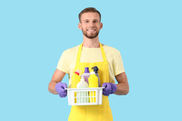 Poster - Male janitor holding basket with cleaning supplies on blue background