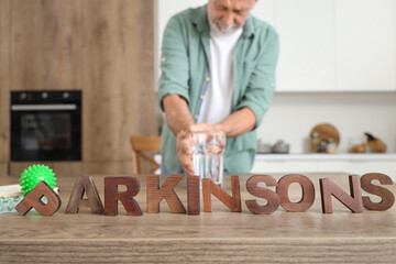 Sticker - Word PARKINSON'S and senior man taking glass of water from table in kitchen, closeup