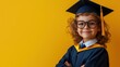 © ZHIJIAN - A cheerful portrait of a child boy wearing a graduation cap and gown, standing against a vibrant yellow background. symbolizing diversity group, graduation, and education.