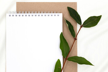 festive background, white blank sheet of notepad with copy space and  sprig of green plant with leaves on delicate silk texture