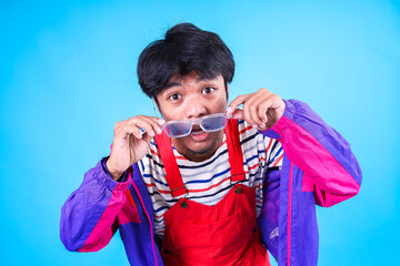 Shocked Asian Man in Colorful Trendy Clothes Holds His Eyeglasses Isolated on Blue Background