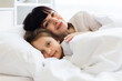 © sofiko14 - Mother and daughter snuggling under white covers, sharing tender moment in bed. Warm, intimate scene displaying family love, comfort, and bonding in clean, cozy bedroom setting.