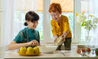 © Westend61 - Smiling woman with son pouring apple into bowl at kitchen