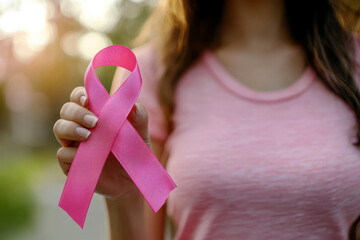 Woman hand holding a pink ribbon for breast cancer awareness on blur background.