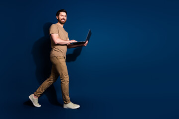 Photo portrait of brunet hair walking man in beige t shirt holding modern laptop working online isolated on dark blue color background