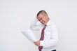 © Mdv Edwards - A middle aged asian manager feeling frustrated after reading disappointing figures on a piece of paper. Scratching his head in exasperation. Isolated on a white background.