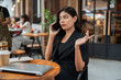 © bongkarn - Uncertain, thoughtful Asian businesswoman is talking on the phone while sitting at a table of a cafe