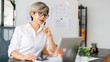 © Pichsakul - A female architect is sitting at her desk, thoughtfully analyzing design plans on her laptop, surrounded by design materials and project documents