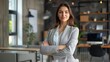 © JINGWEN - Confident businesswoman with crossed arms smiling in modern office, facing camera, embodying success in professional attire with sleek hairstyle.
