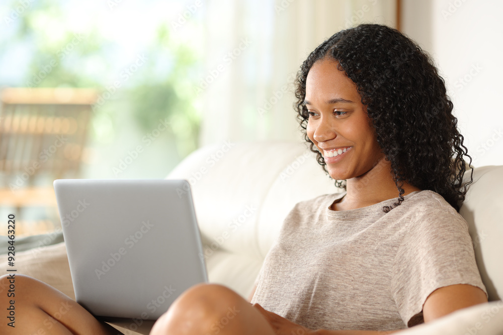 Happy black woman checking laptop on a sofa Stock Photo | Adobe Stock