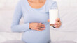 © Prostock-studio - Dairy In Pregnancy Diet. Unrecognizable Pregnant Woman Offering Glass Of Milk To Camera Sitting On Bed In Bedroom. Cropped