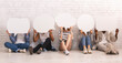 © Prostock-studio - Group of young people sitting on floor over white brick wall, covering faces with speech bubbles, panorama