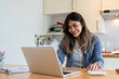 © wichayada - Young Woman Working as a Freelancer from Home on Laptop in Modern Kitchen Setting, Smiling and Engaged in Her Work