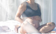 © puhimec - Pregnant woman touches big belly while sitting on bed.