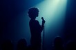© antusher - Person holding microphone facing audience, silhouette effect with spotlight.