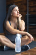 © puhimec - A pregnant woman in the gym sits on a mat and drinks water.